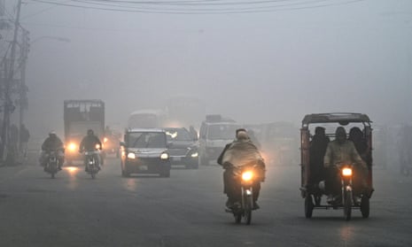 Commuters make their way along a street amid dense smog in Lahore