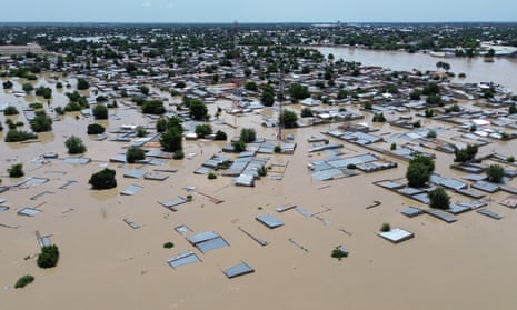 aerial view over houses submerged under brown, muddy water with flooding across a large swathe of the town