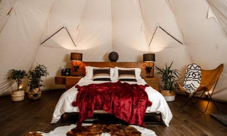 A luxurious double bed in a tipi, with a plush red velvet throw on it. 