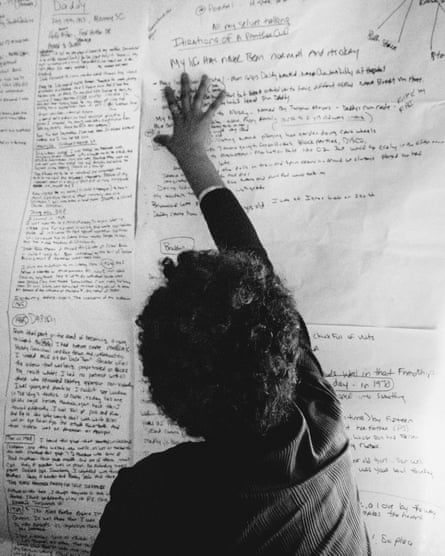 K’Sisay Sadiki has her hand up against the wall where large sheets of paper covered in small handwriting are posted.