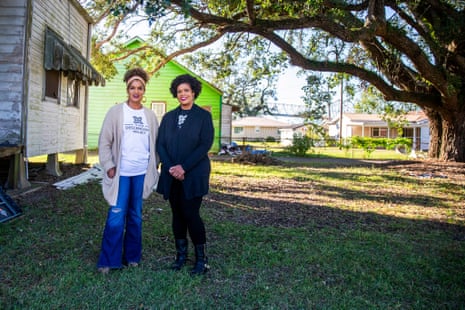 Two Black women stand in front of a house beyond a massive oak tree.
