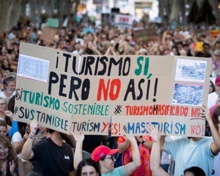 Protesters in Mallorca hold a cardboard sign reading