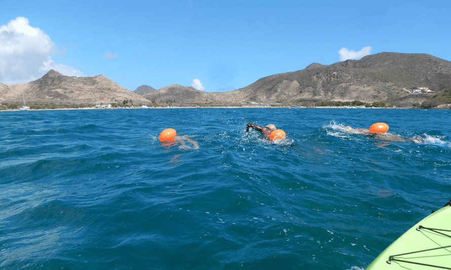 Three swimmers in the sea at St Kitts, mountains in the background