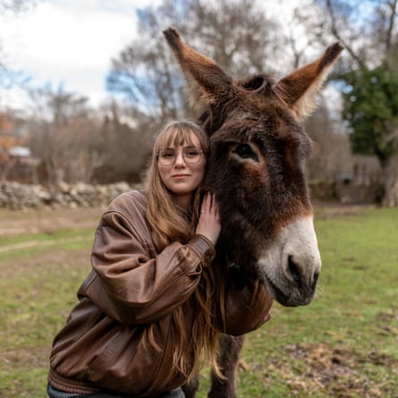 Young woman with glasses and leather jacket embracing a donkey in a field