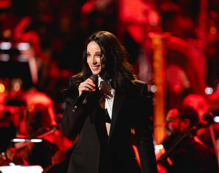 St Vincent singing at the proms, with the orchestra blurred out with a red tint behind her