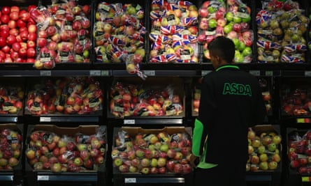 An Asda employee in front of shelves stacked with apples