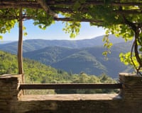 Grape vines on a veranda pergola frame a view of forested hills near Saint-Hilaire-de-Lavit