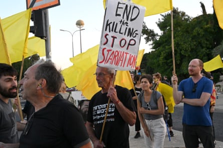 A man holds a handmade sign reading “END THE KILLING STOP THE STARVATION” during a protest