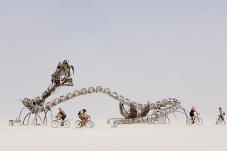 People bike around a skeletal art structure in a desert