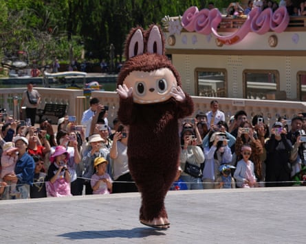 A person in a Labubu mascot costume performs on stage as a crowd of people look on