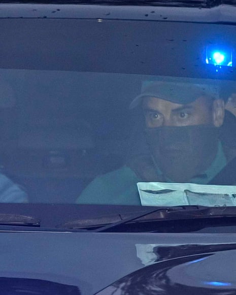 Daniel Kinahan sitting in the back of unmarked police car with a blue light, his face partially obscured by the person in the front seat