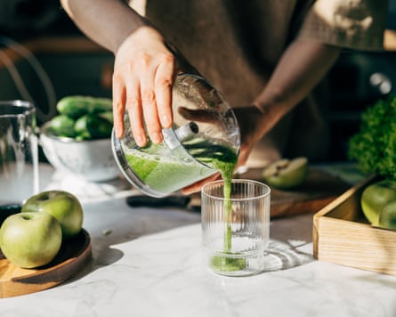 A person pouring a green smoothie into a glass