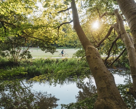 A woman on a bike cycling past a pond with a sunset seen through trees
