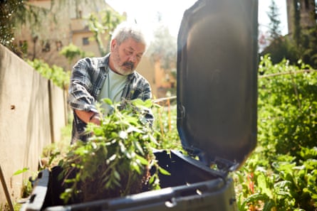 An older man with a beard is adding materials to a compost bin