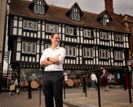 Hamish Falconer in a street in front of Tudor buildings