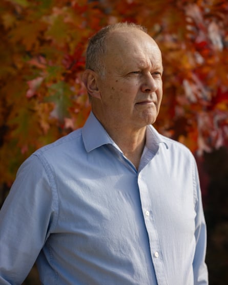 Chris Moore pictured from the waist up, standing in front of a tree with red leaves, looking off camera