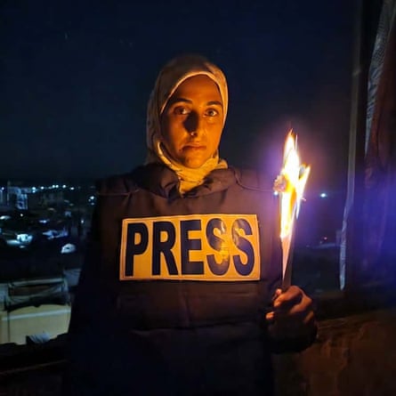 Malak A Tantesh wears a ‘Press’ vest and holds a burning piece of paper in tribute to journalists killed.