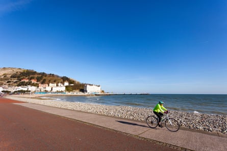 Seorang pengendara sepeda sendirian yang sedang bersepeda di pagi hari di sepanjang pantai dan trotoar.