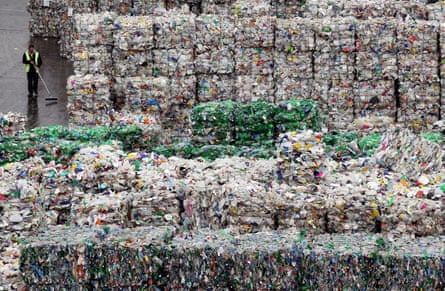 A worker at a recycling plant in Dagenham, London, walking past stacks of plastic bottles.