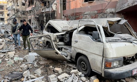People walk through rubble and by a damaged vehicle in southern Beirut.
