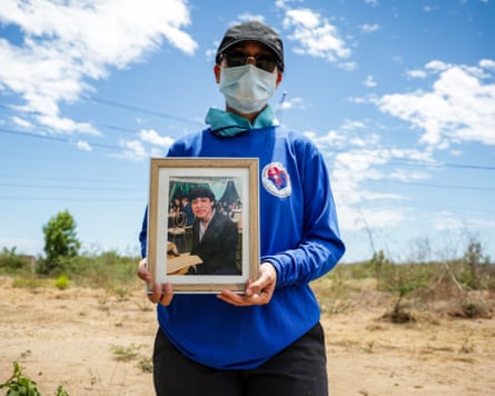 A woman in a face mask and vlue shirt holds a picture of a young man.