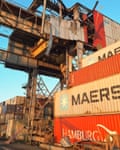 Damaged metal work on a sheetmetal structure above stacked Maersk and Hamburg shipping containers