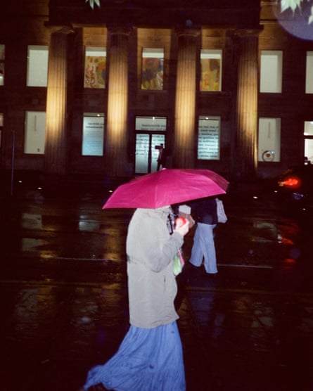 Una mujer camina rápido sosteniendo un paraguas rosa.
