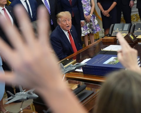 Reporters raise hands as President Trump speaks at his Oval Office desk