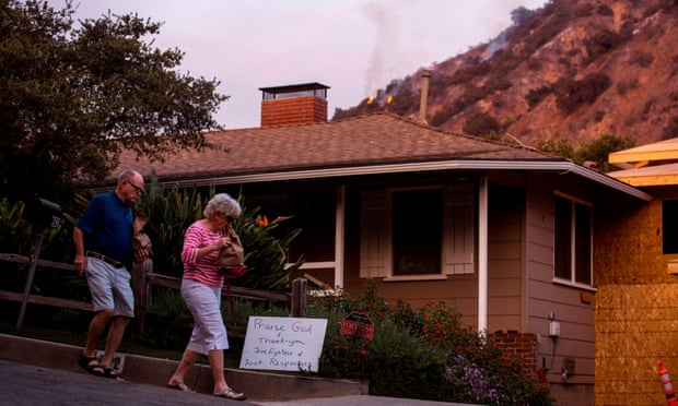 People walk past a sign thanking firefighters and first responders as they return home, as smoke from the Bobcat Fire burning in the San Gabriel mountains rises above, in Monrovia, California, last week.