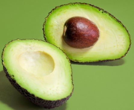 Avocado sliced into two halves against a green background.