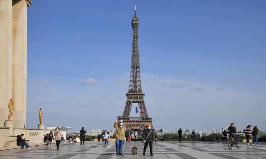People are seen standing near the Eiffel Tower in Paris, France. 