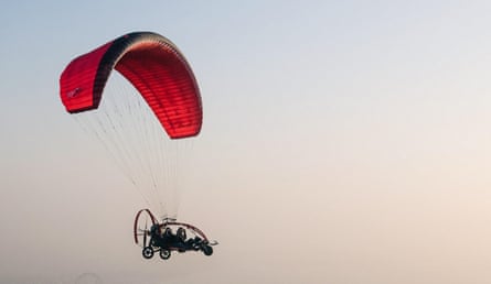 Paramotor with a red wing in flight, carrying two people