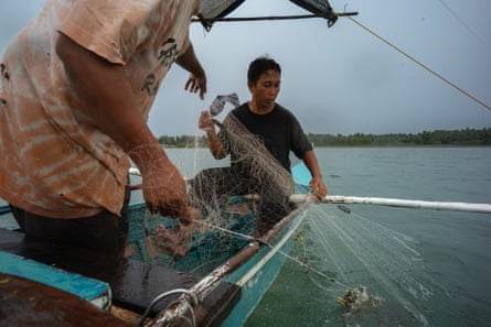 Two men in a boat haul a net from the water