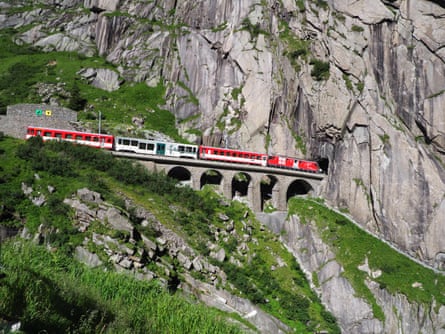 Red train on scenic stony St Gotthard railway bridge and tunnel, swiss Alps
