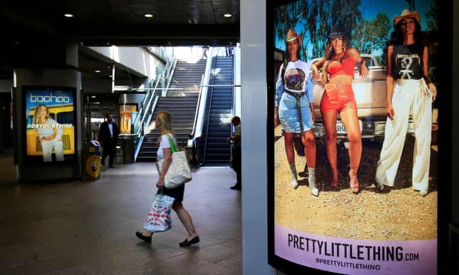 A shopper walks pass advertising billboards for Boo Hoo and for Pretty Little Thing.