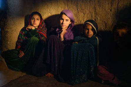 Three girls sit against a wall in a dark room. A shaft of light illuminates their faces.
