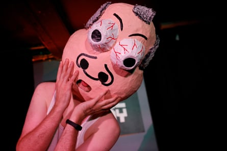 A man wearing a white vest and a large oversized papier mache head