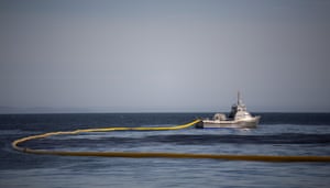 A boat places boom containment line around an oil spill in an attempt to limit the damage.