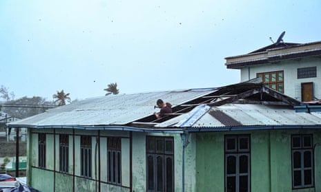 A man uses a hammer to repair a roof damaged by Cyclone Mocha