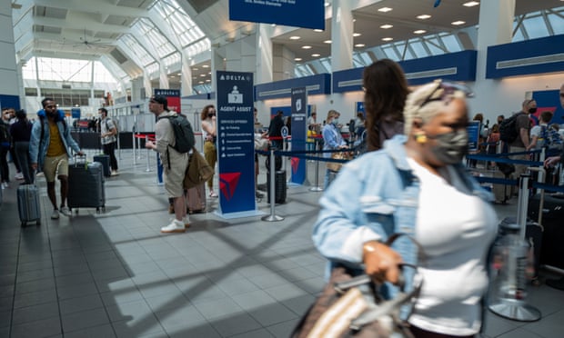 A woman with sunglasses perched atop her head and pulling a suitcase is seen blurred at right as she rushes through a terminal filled with travelers.