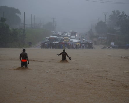People wading waist deep across what looks like muddy river towards halted rows of cars
