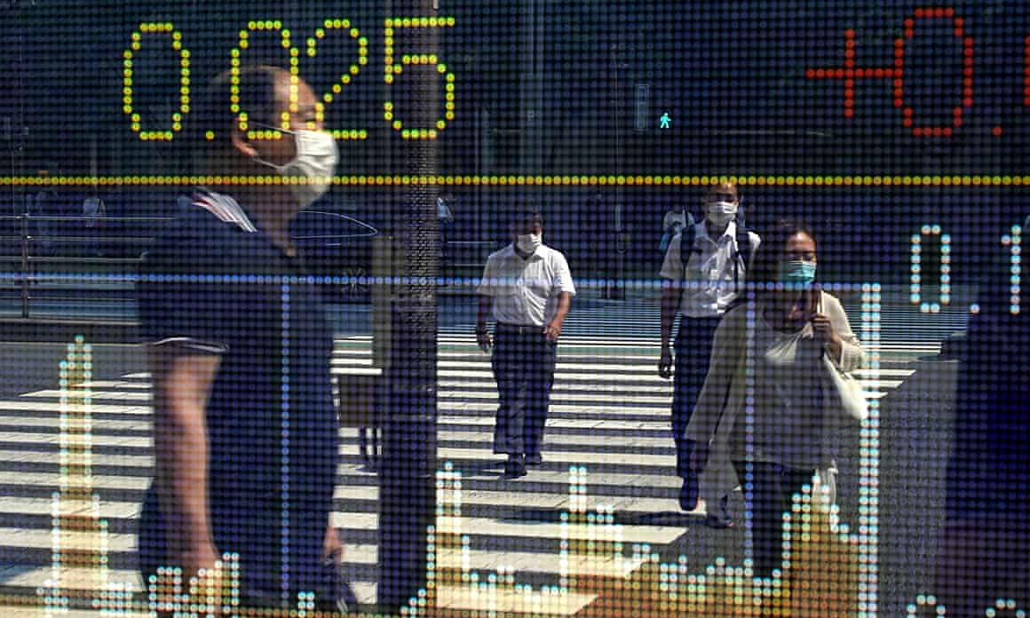 People walking across a zebra crossing in Japan are reflected in a window displaying digitised stock market figures