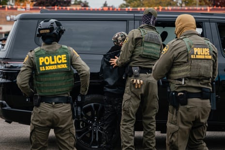 masked federal agents move a detained man into a vehicle