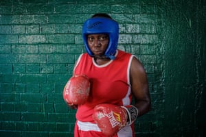 Damilola Adigun in blue headguard, red gloves and vest, against brick wall background.