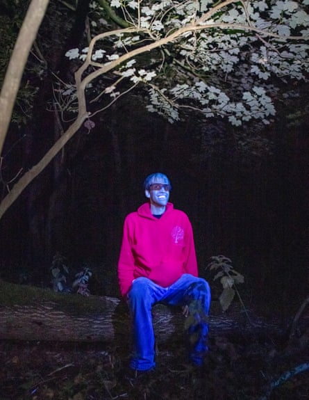 David Atthowe sits on a branch smiling while lit up by UV light at night. His skin looks grey in the light