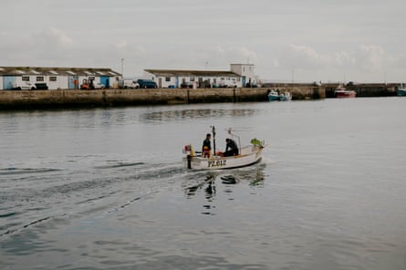 Two people in a small fishing boat in a calm harbour.