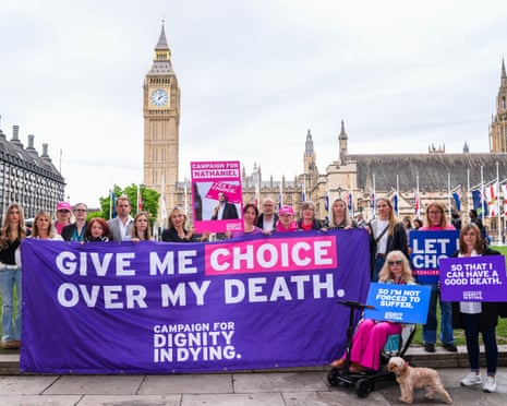 A group of protesters stand behind a banner which reads: 'Give me choice over my death'. The Houses of Parliament can also be seen in the background