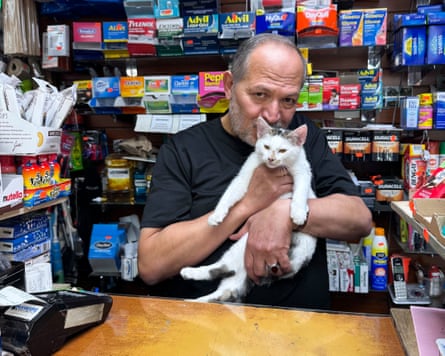 Man behind a bodega counter snuggling his cat