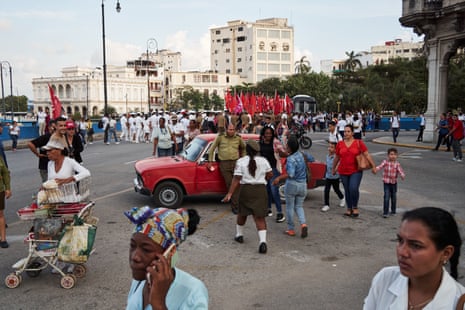 People go about their business in a Havana street while a military parade goes by