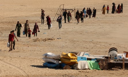 A line of people carrying belongings stretches back along a beach